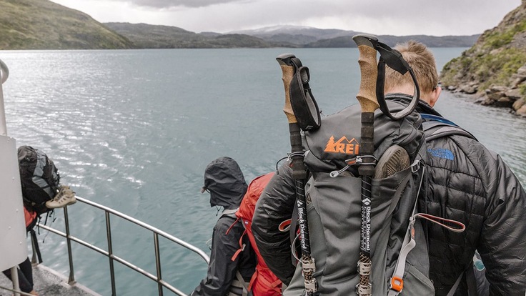 People dressed in hiking gear on the edge of a boat looking out over water, with land in the distance.