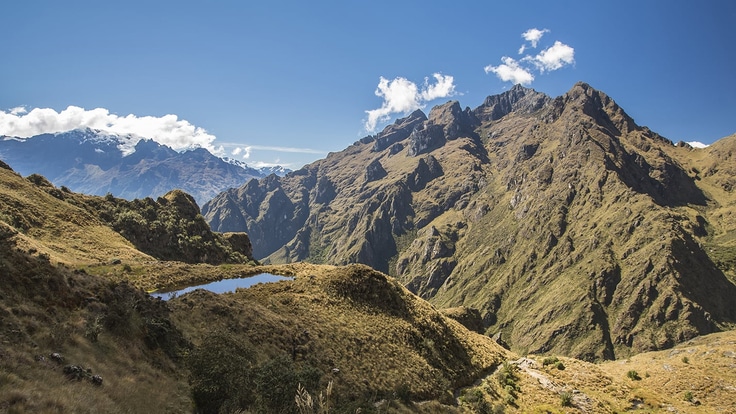 An alpine lake shines under a blue sky in a remote and verdant mountain range