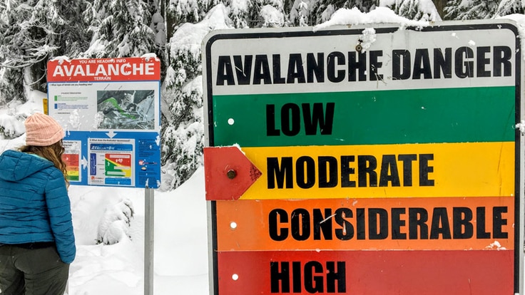 A person reads a sign about avalanche danger in the backcountry