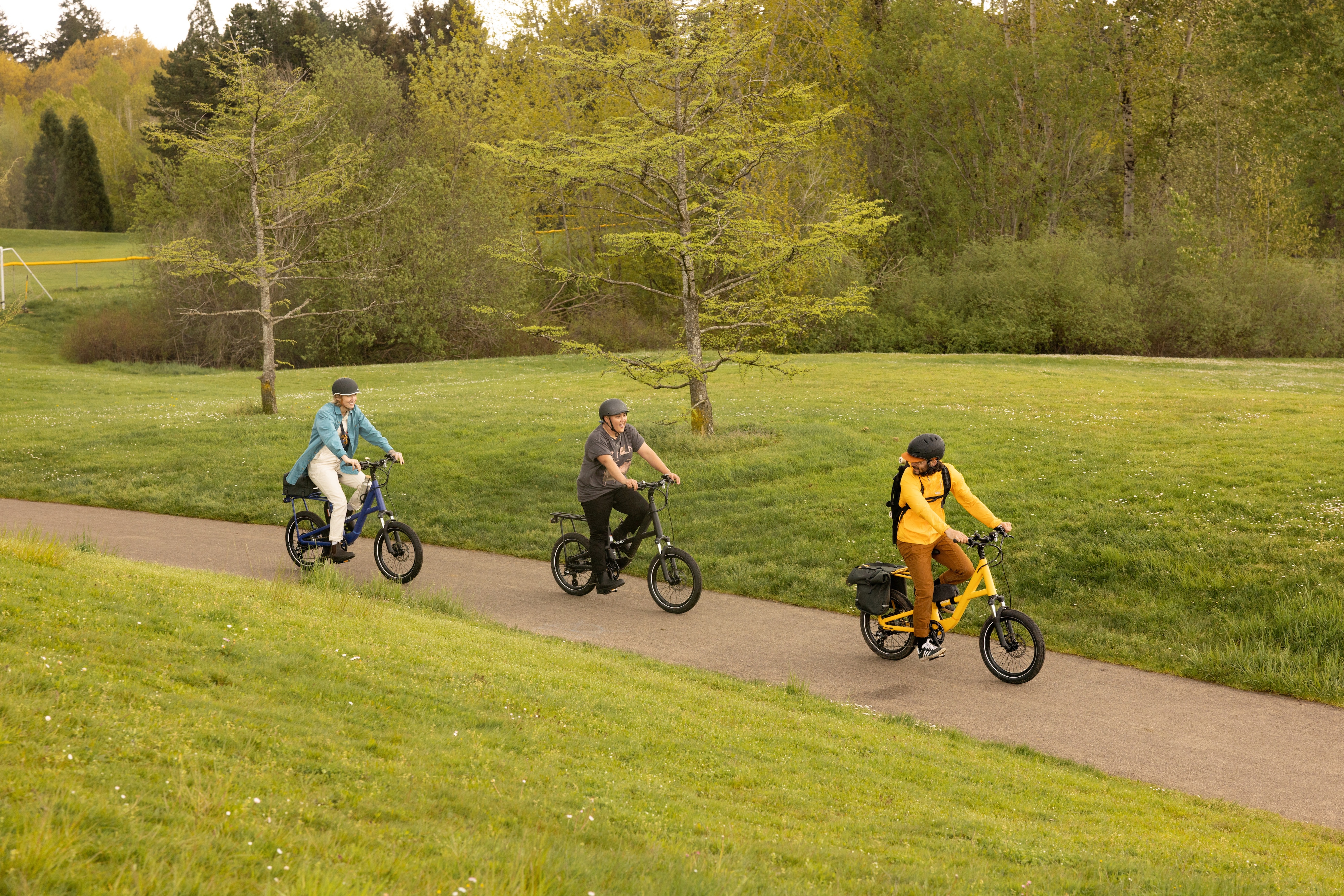 Three cyclists ride along a bike trail through a park.