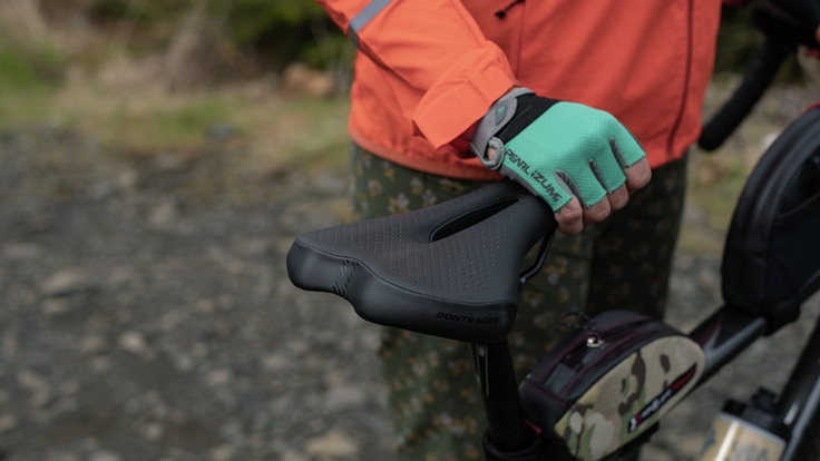 Cyclist standing next to bike with gloved hand on black saddle.