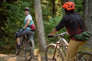 Two people mountain biking in a forest with cycle clothing and accessories
