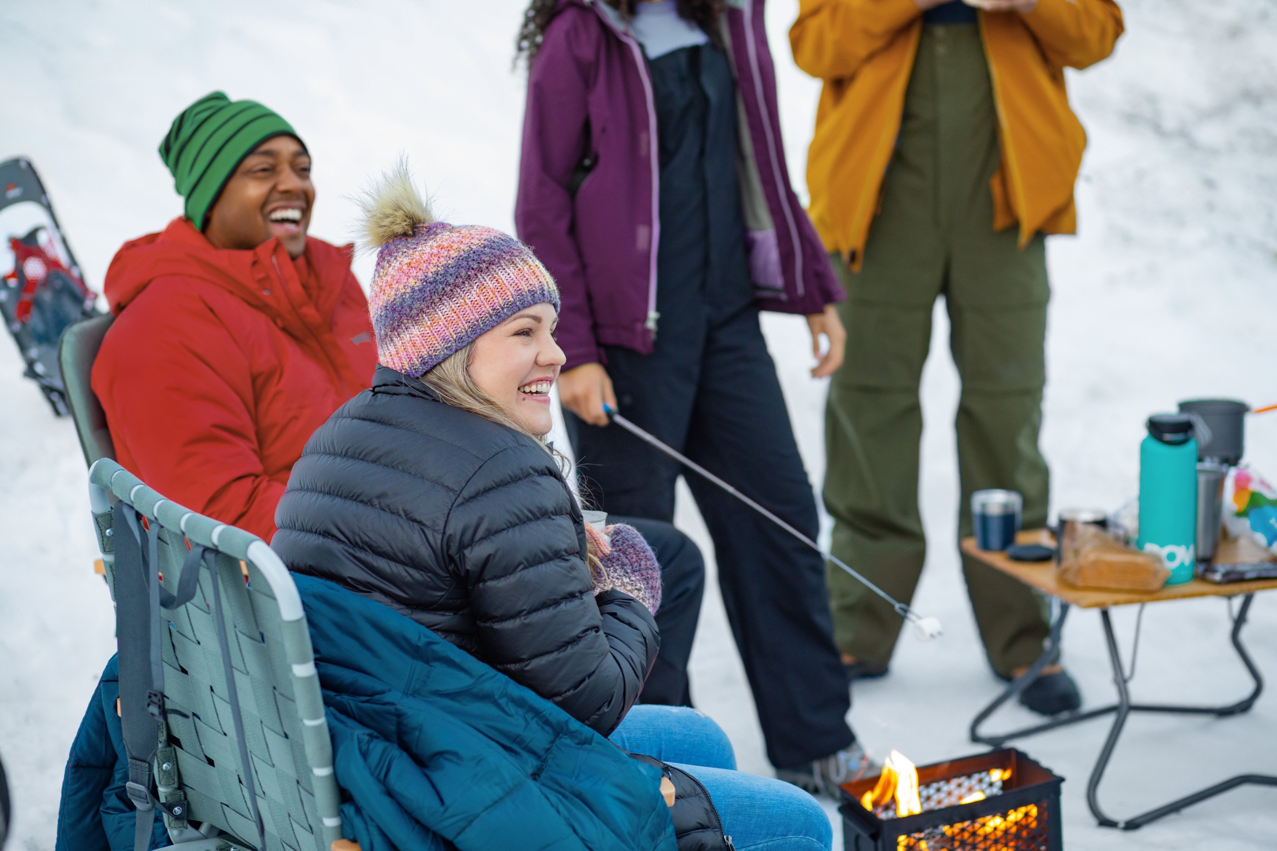 Campers roast marshmallows around a campfire in the snow.