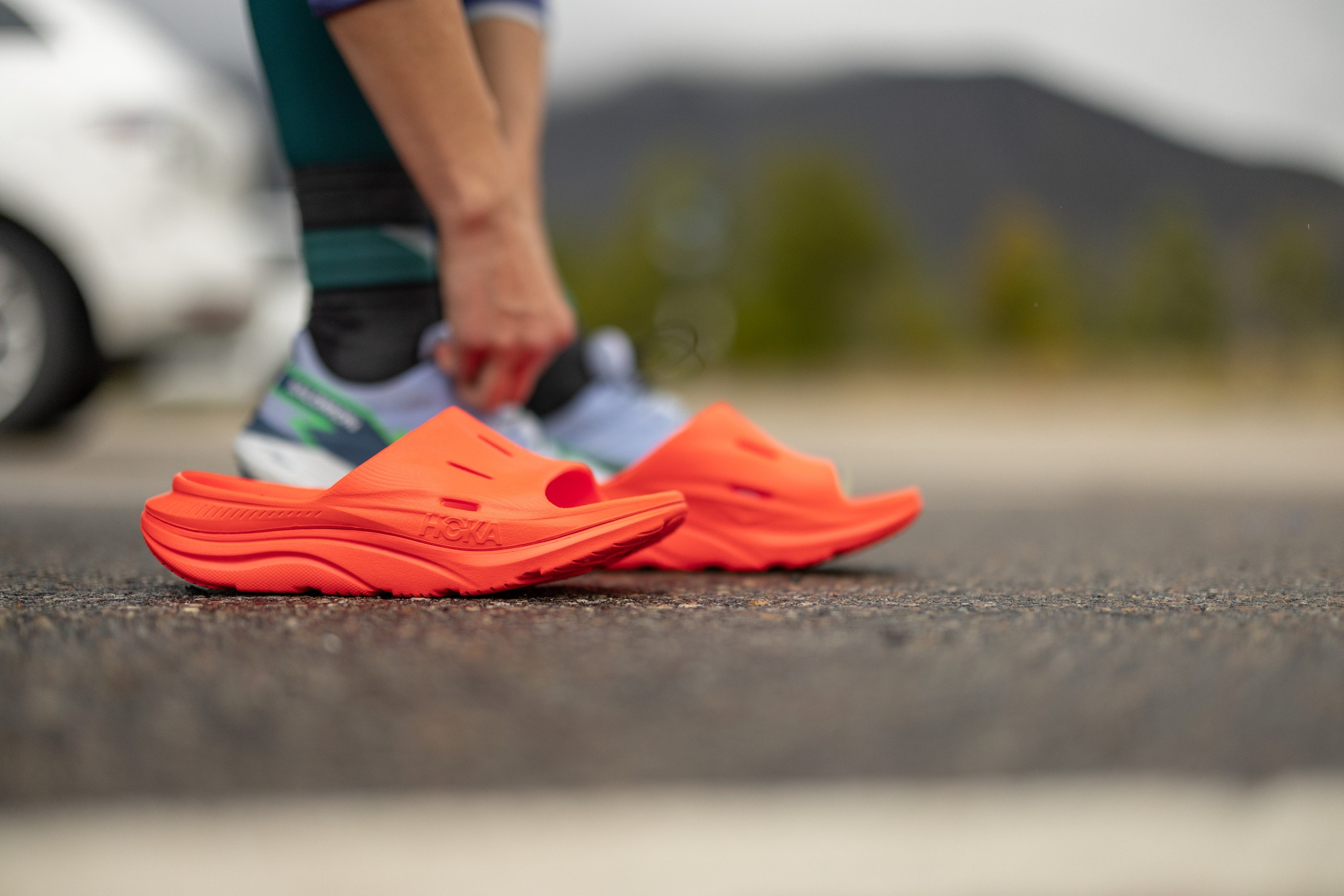 A runner puts on an orange pair of HOKA ORA Recovery 3 Slides