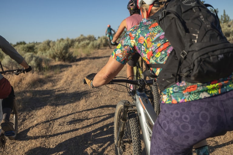 A mountain biker wearing a black backpack rides a dirt trail