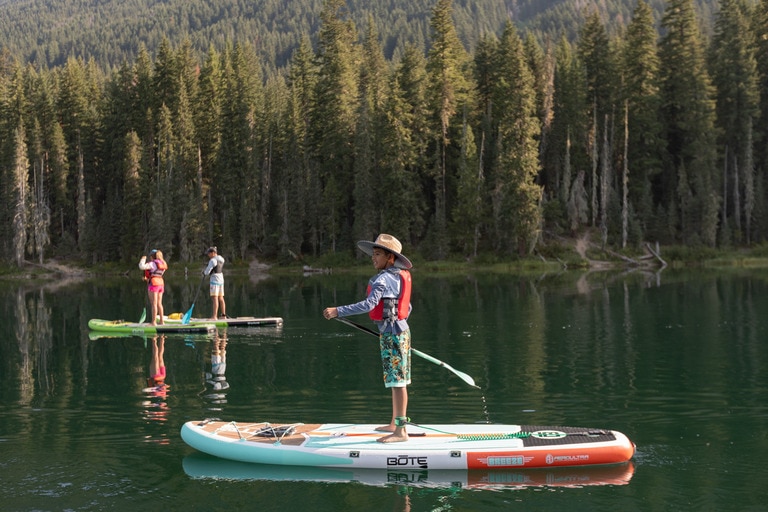A child paddles on an inflatable paddle board on a calm lake