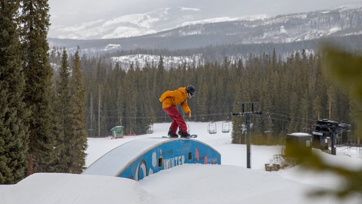 A snowboarder does a trick on a feature in a terrain park