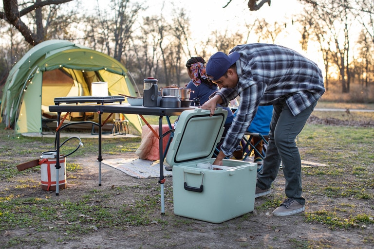 A person at a campsite reaches into a YETI cooler.