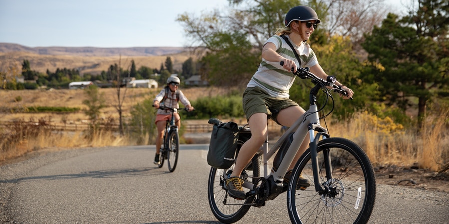 Two women riding ebikes climbing a hill top.