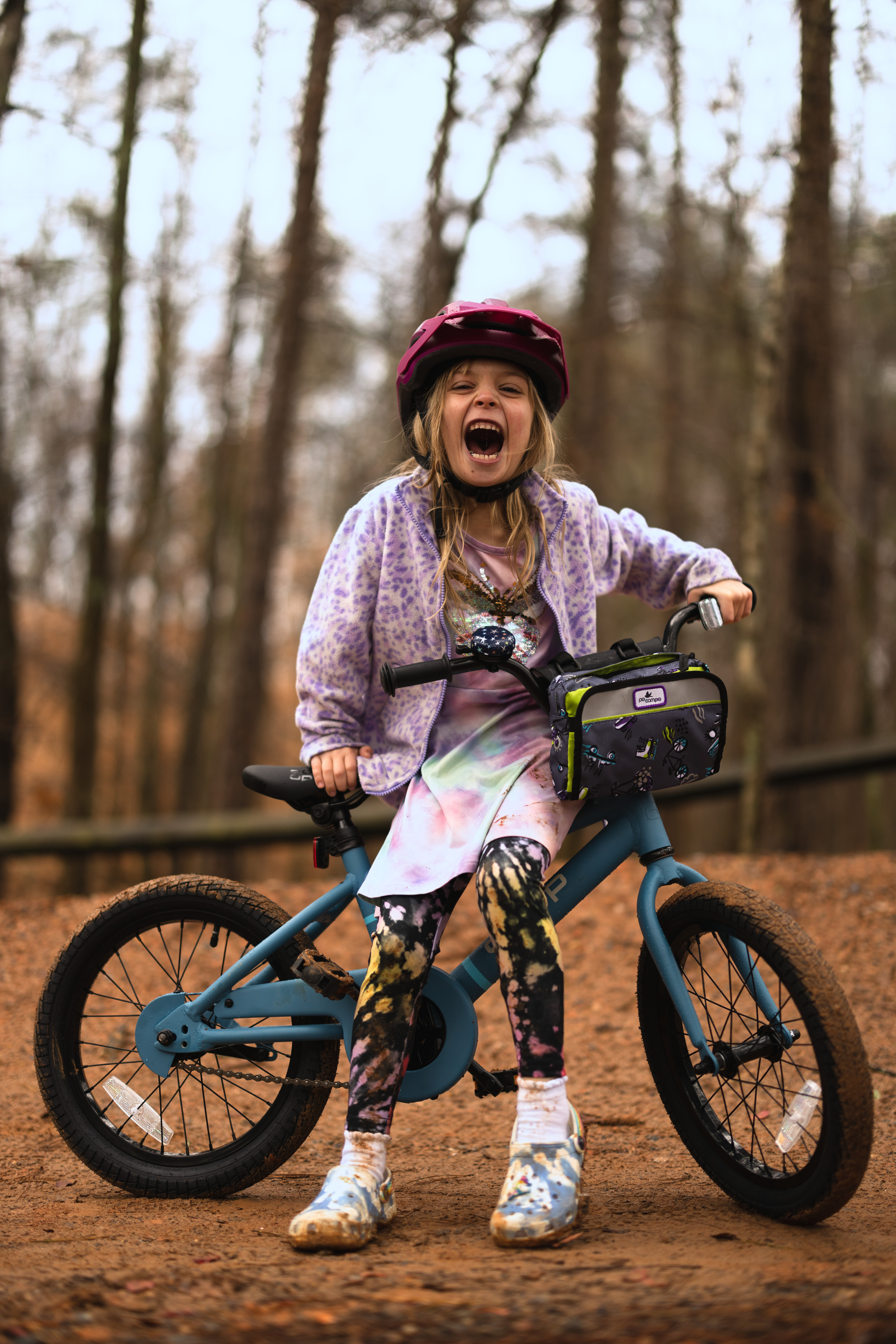 A child laughs for the camera while sitting on their bike.