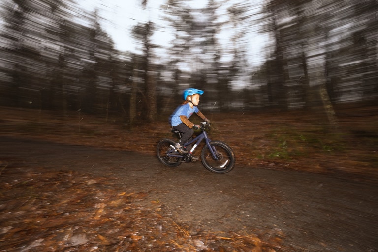 A young kid in a blue helmet rides a mountain bike on a trail. 