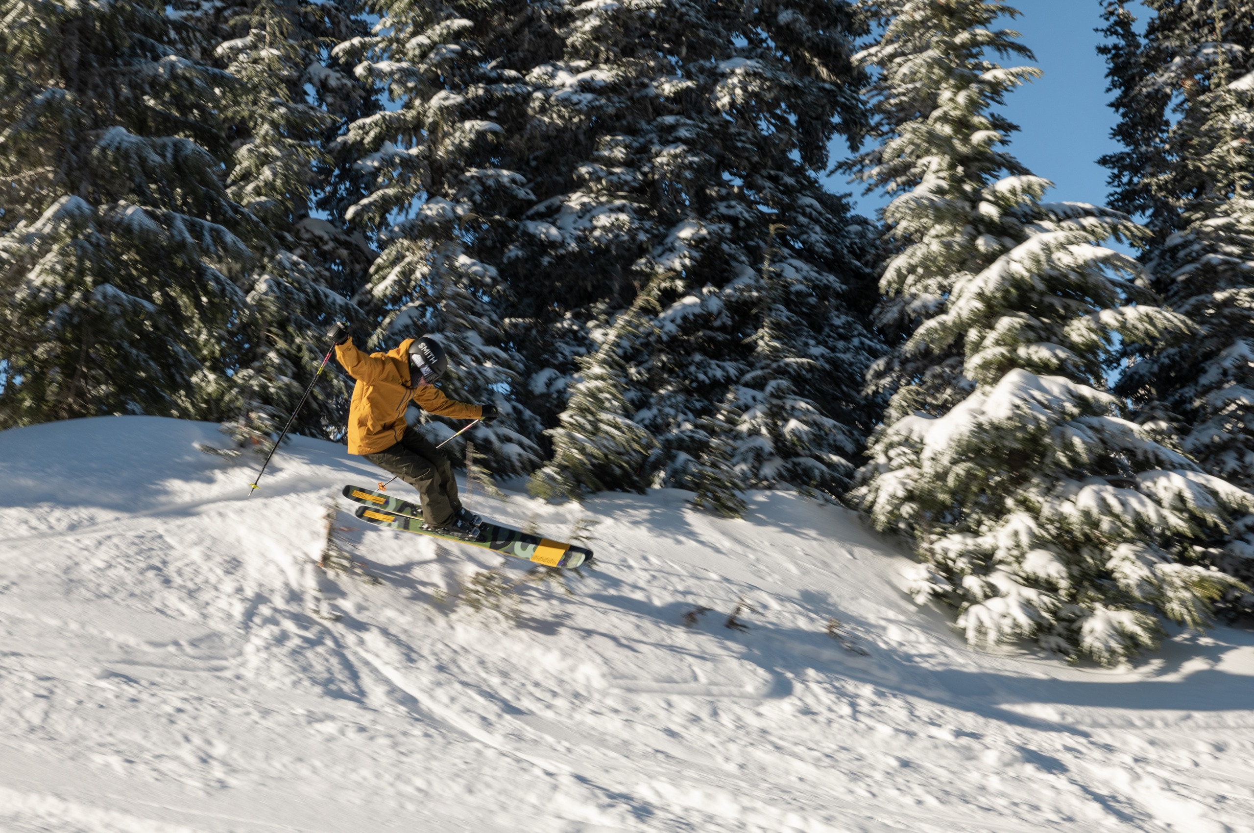 A skier hits a small jump on a run at the local ski resort.