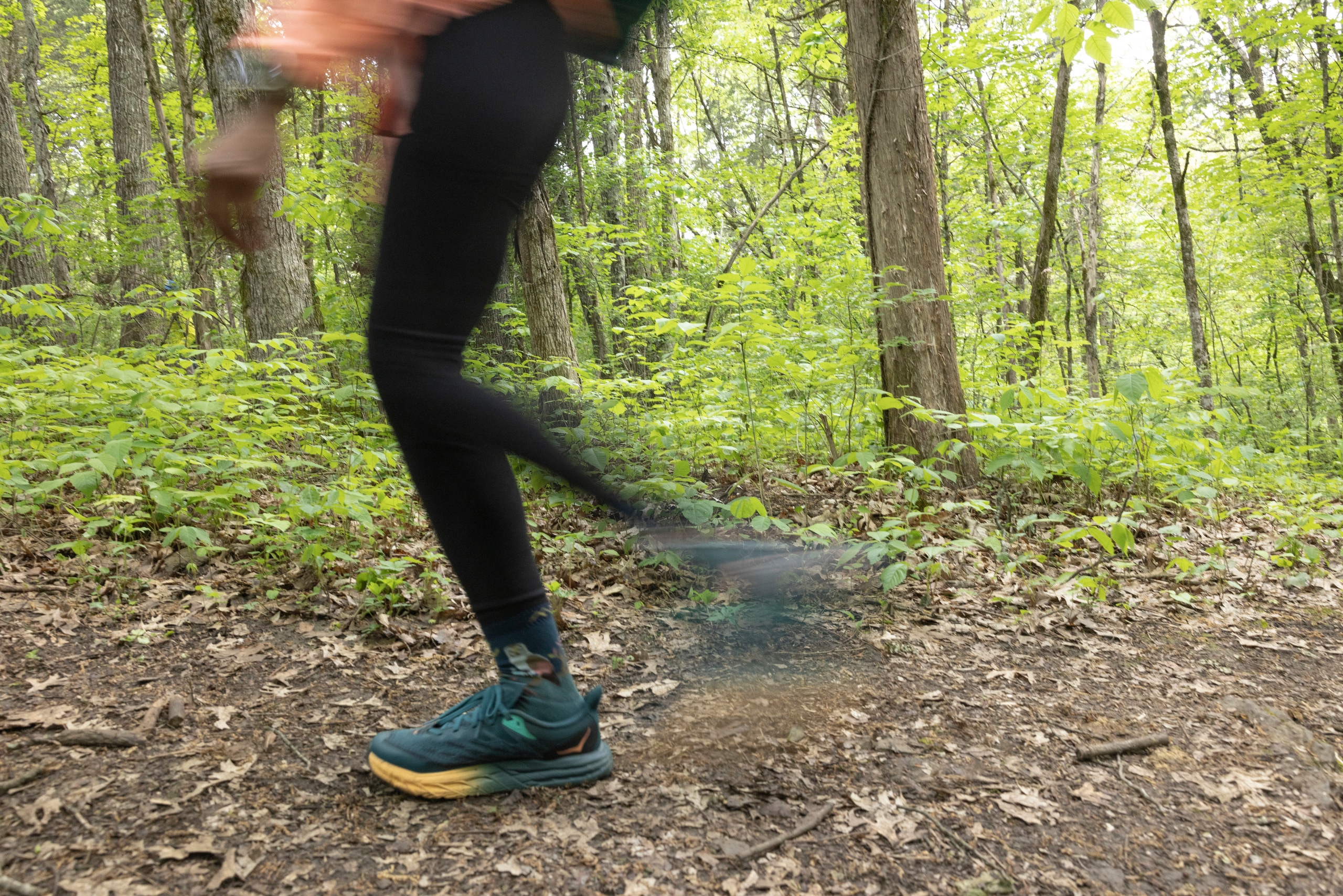 A fast-moving hiker passes by in a blur through a forest, with only their hiking shoes in focus in the image