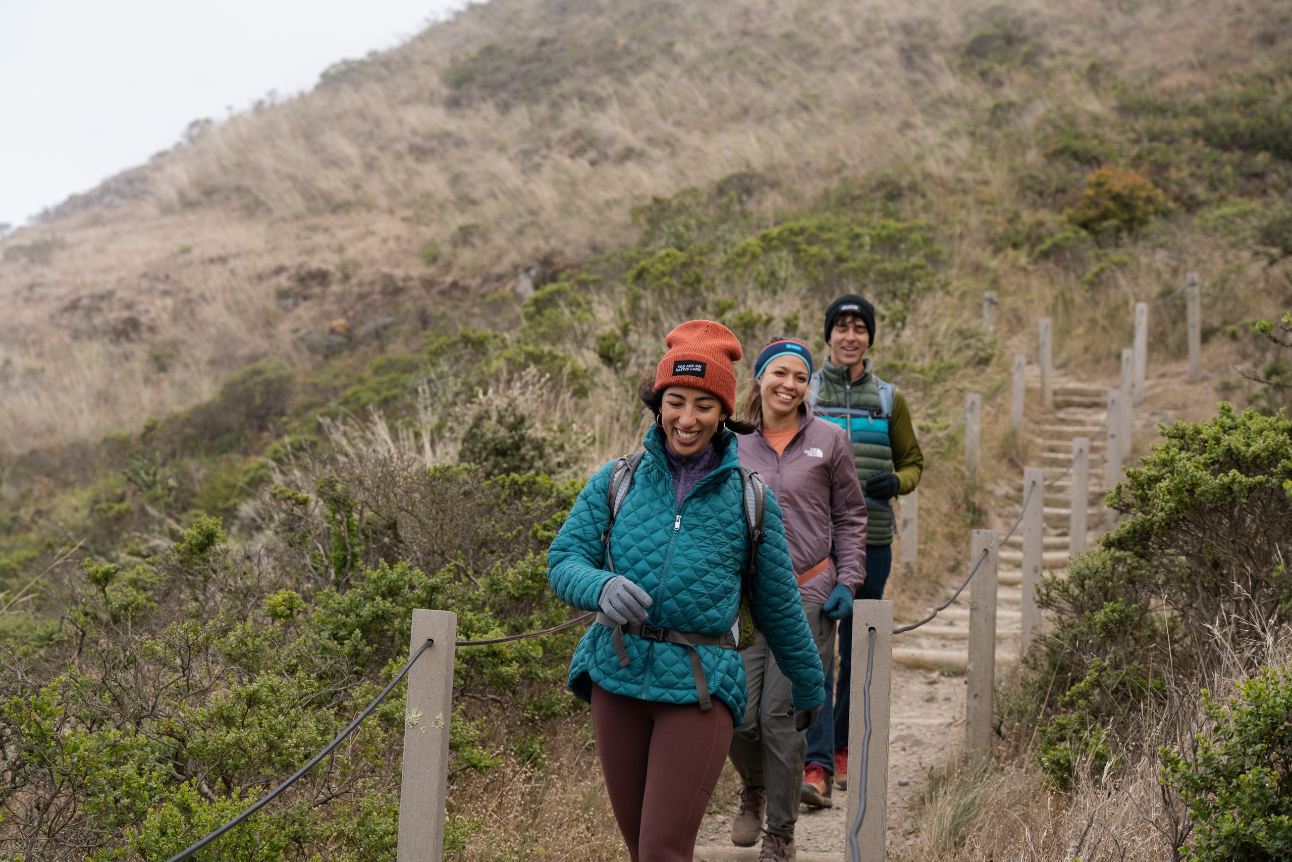 Three hikers smile while trekking along a trail
