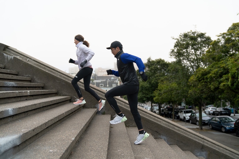 Two runners wearing gloves head up steps in winter