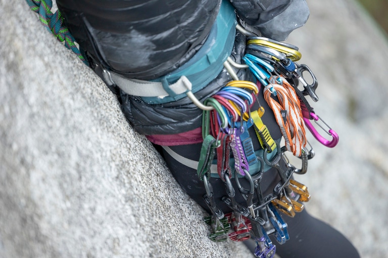 Carabiners, slings and cams hang off the loops of a climbing harness.