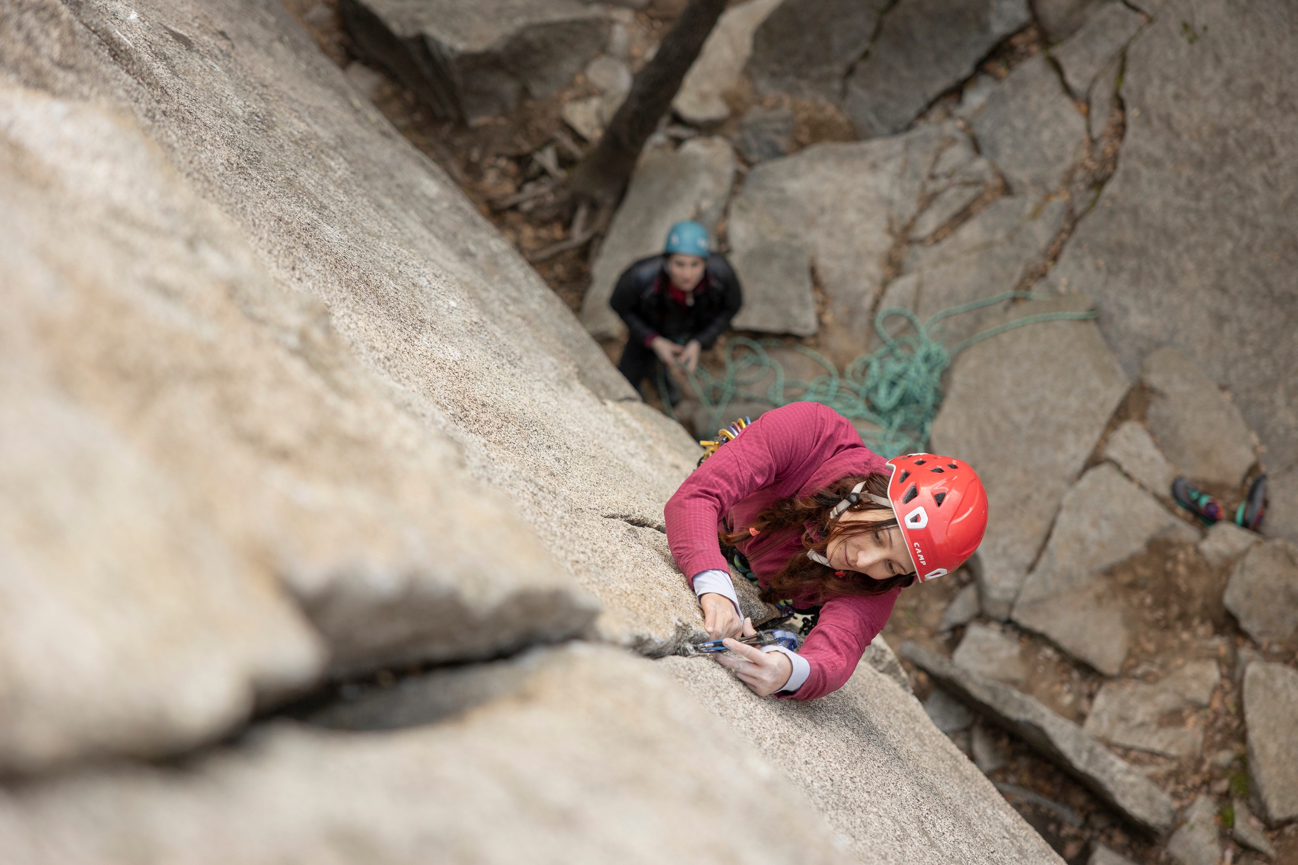 A climber places protection into the crack of a rock wall and someone belays below.
