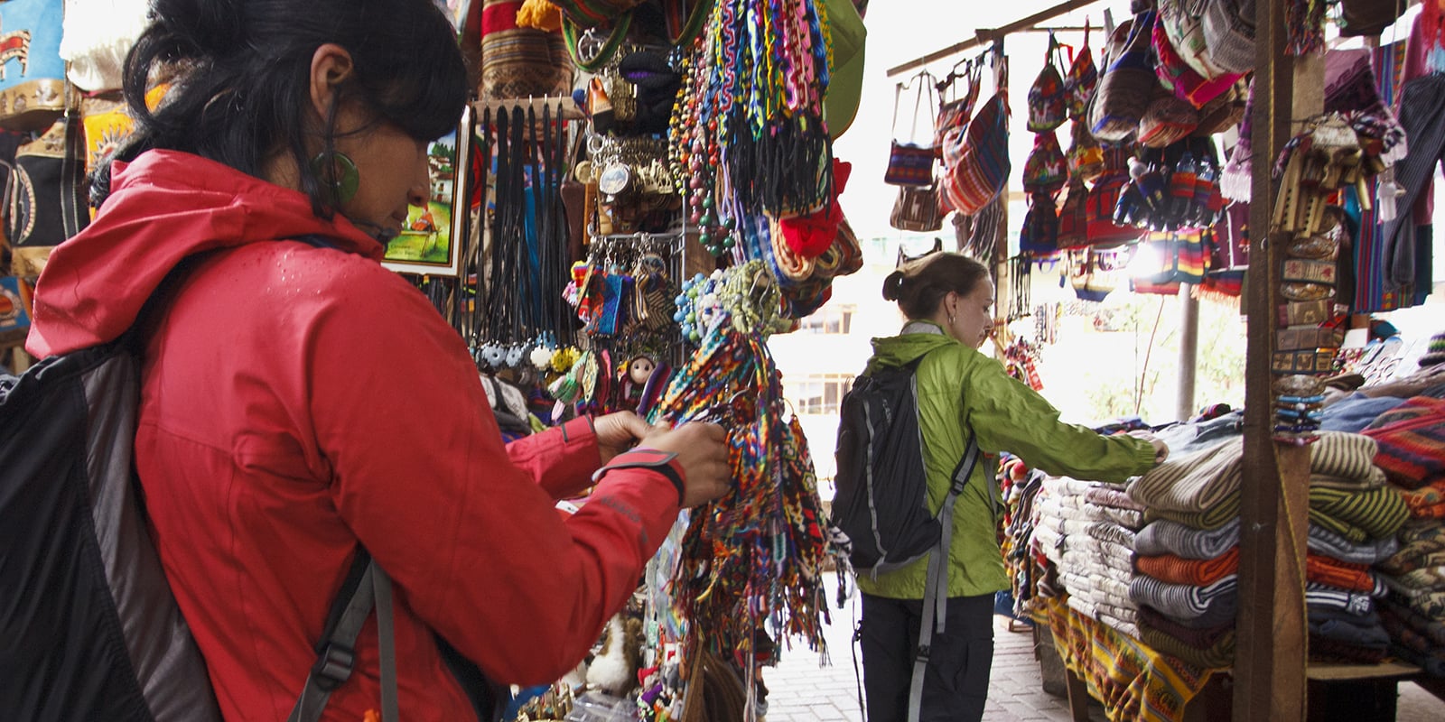 Two travelers looking at blankets and bracelets at an outdoor market.