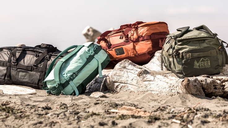 Four duffel bags piled atop some driftwood on a beach