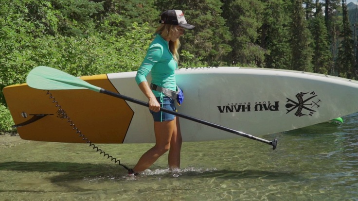 A woman carries her stand up paddle board towards water