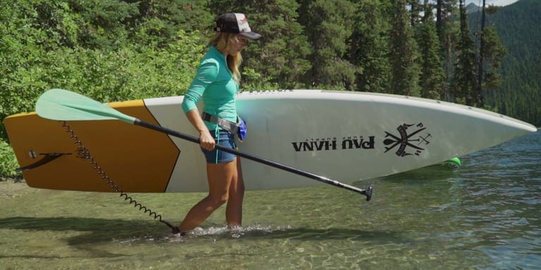 A woman carries her stand up paddle board towards water