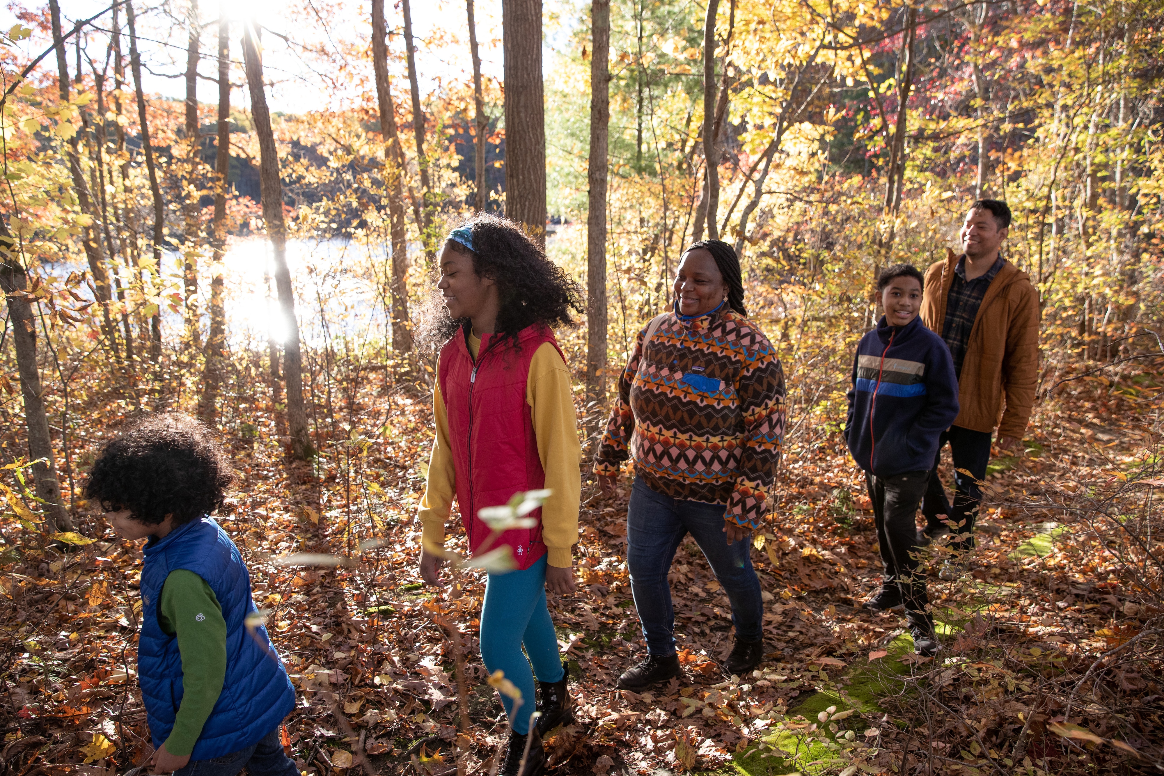 A group of five hikers enjoy a trail through a fall forest.