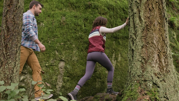 Woman wearing lilac leggings hiking on forested trail, followed by another hiking companion