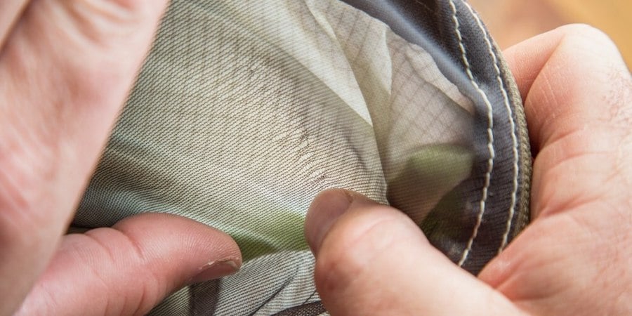 A person's thumb working the mesh strands back together on a tent window