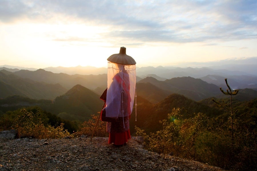 Woman under an umbrella on a mountain trail at sunrise.