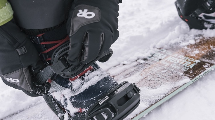 A snowboarder straps into his bindings