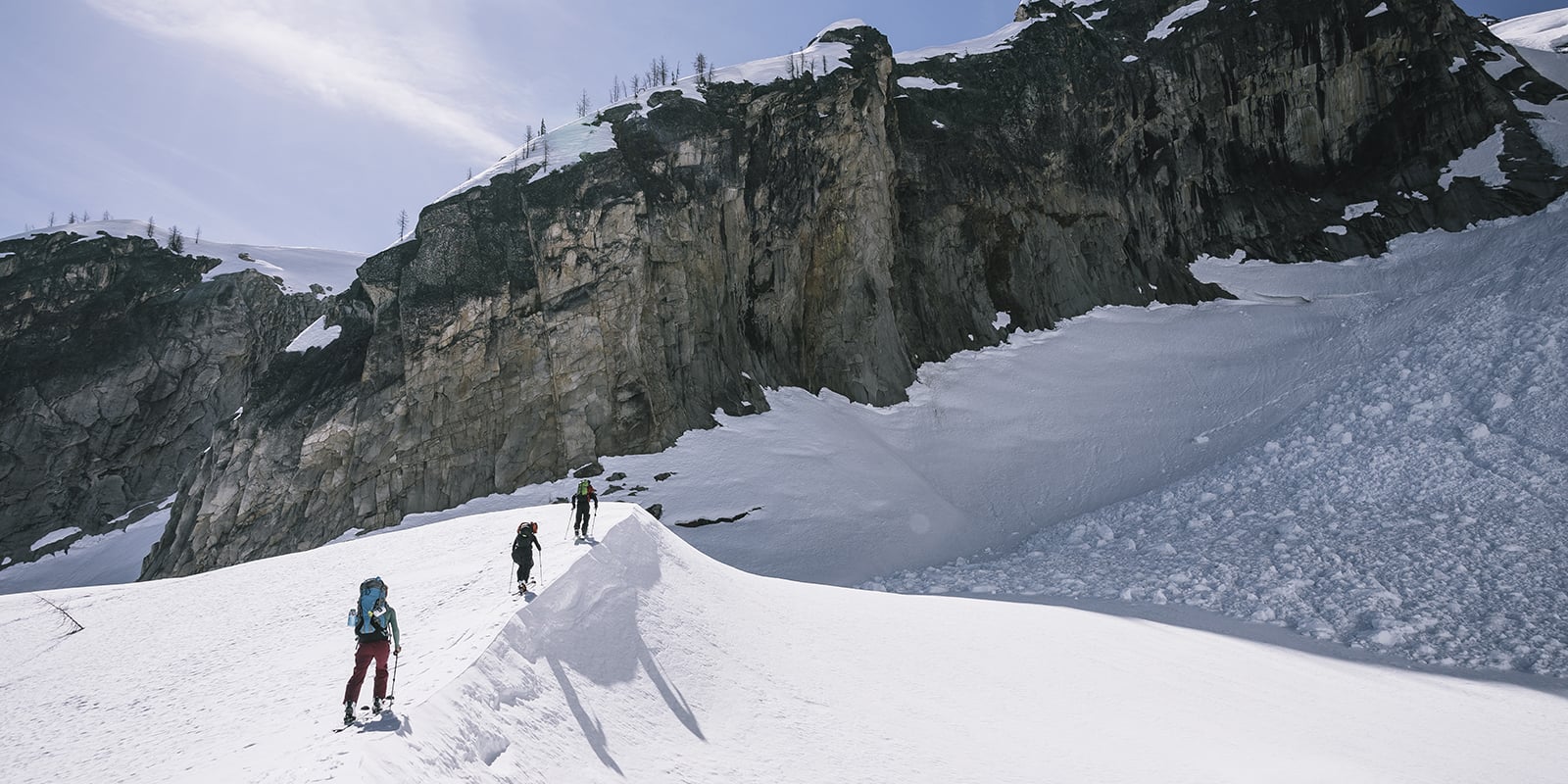 wide shot of 3 skiers trekking up a mountain on a sunny day