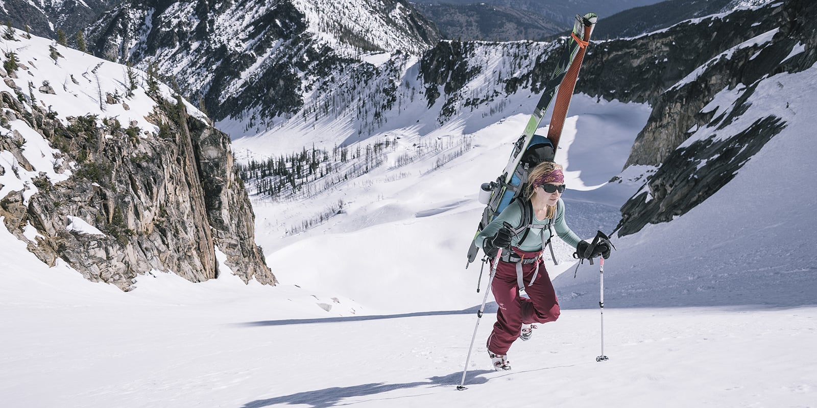 Powder skis strapped to her backpack, a skier hikes up a snowy mountainside