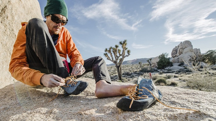 A rock climber sitting down while lacing up climbing shoes in the desert