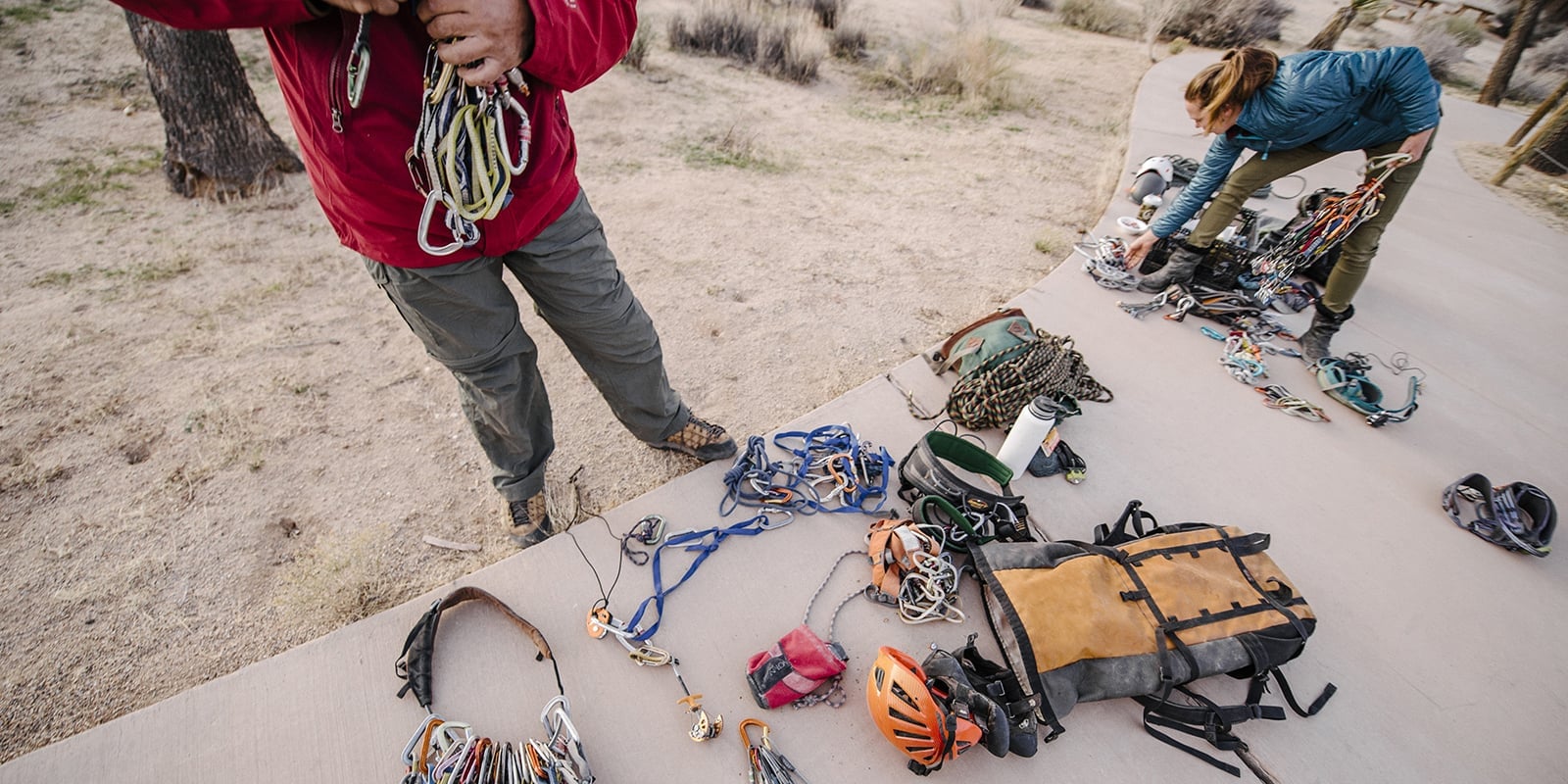 A cement path with climbing gear laid out on it and climbers sorting through all of their gear