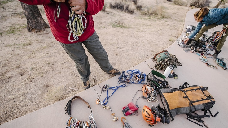 A cement path with climbing gear laid out on it and climbers sorting through all of their gear