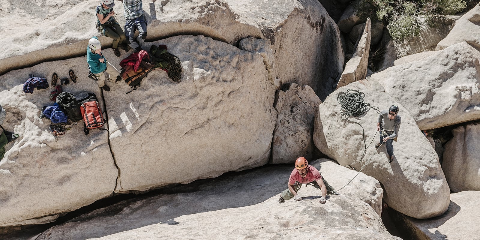 Climber scaling a rock while one person belays and others watch