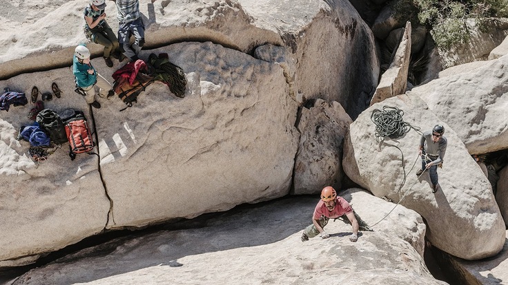 Climber scaling a rock while one person belays and others watch