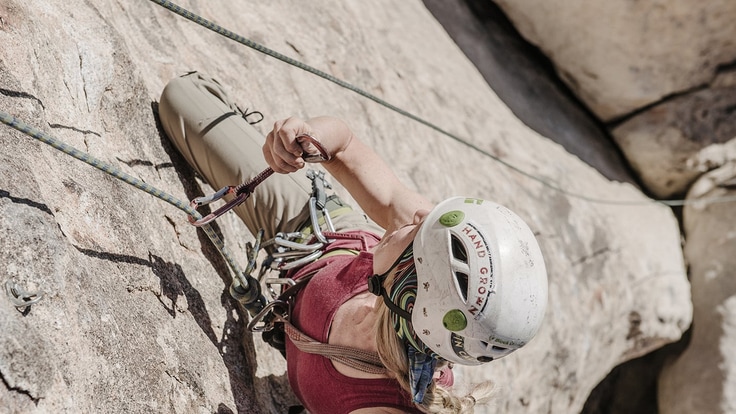 Close up of a woman rock climbing up a rock face wearing a white helmet