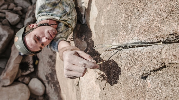 A climber set a pro placement, also known as protection gear, in a rock face