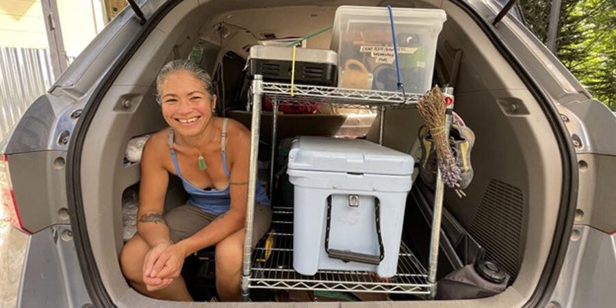Chef Maria Hines sits in the back of her vehicle near a cooler.