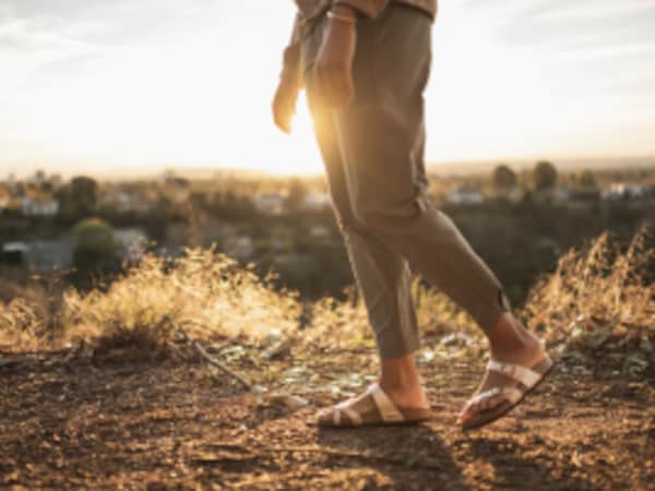A person wearing sandals walks along a desert path as the sun sets.