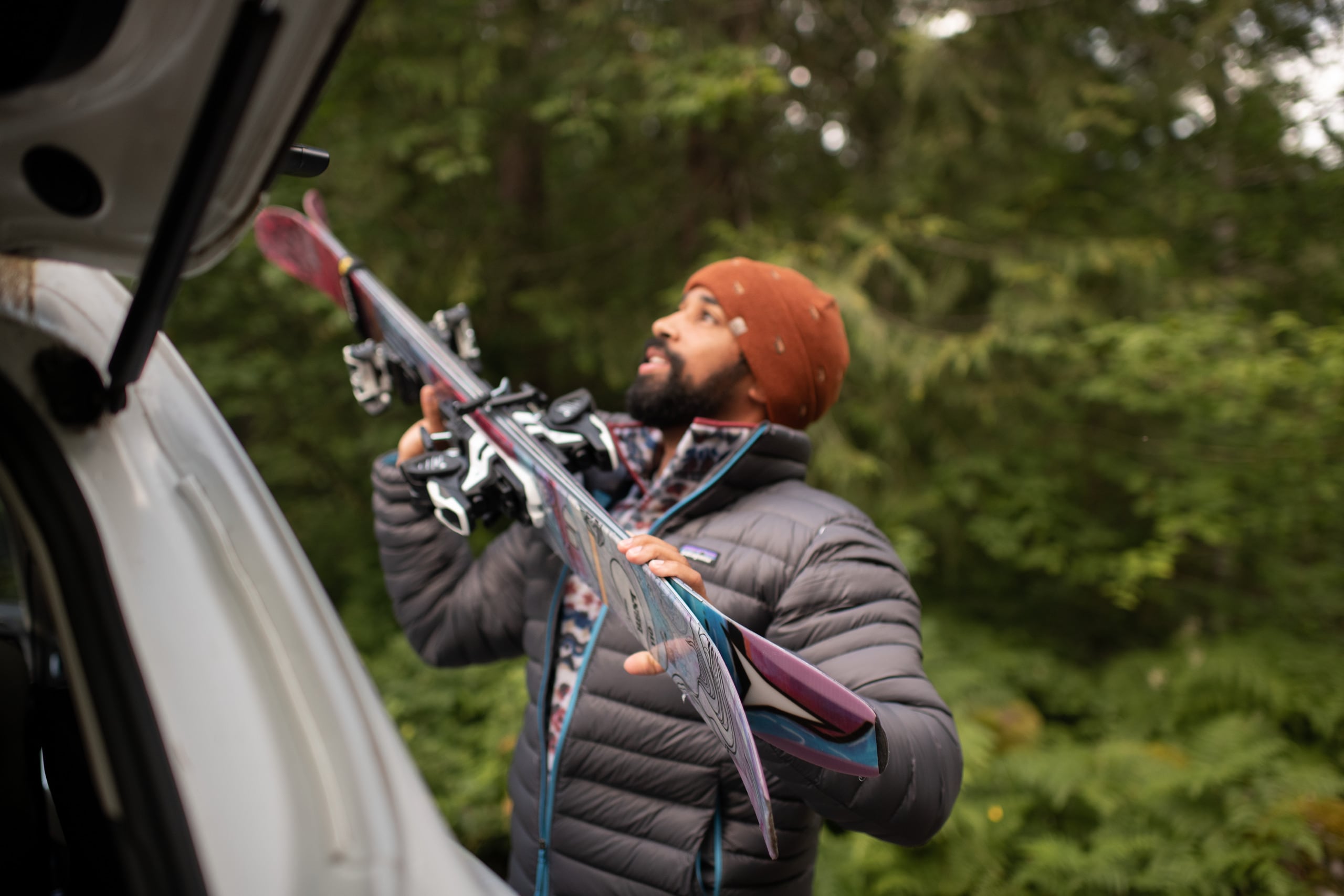 A person wearing a Patagonia down jacket loads skis into a car rack.