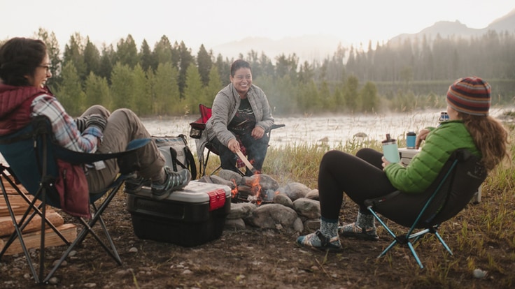Three women sitting around a campfire in camp chairs