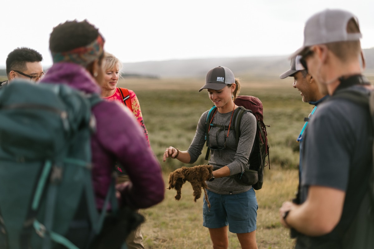 A guide talks to a group of hikers about plants she has picked up in a field