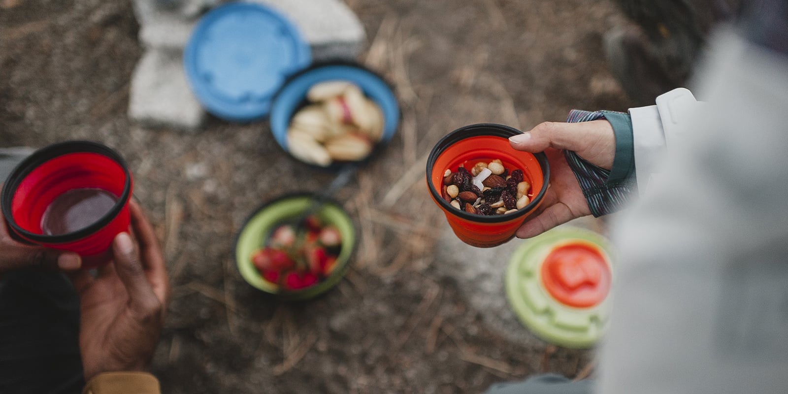 Close up of someone holding a camping bowl of trail mix, more bowls of food in the background.
