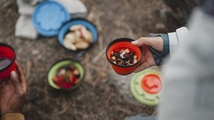 Close up of someone holding a camping bowl of trail mix, more bowls of food in the background.