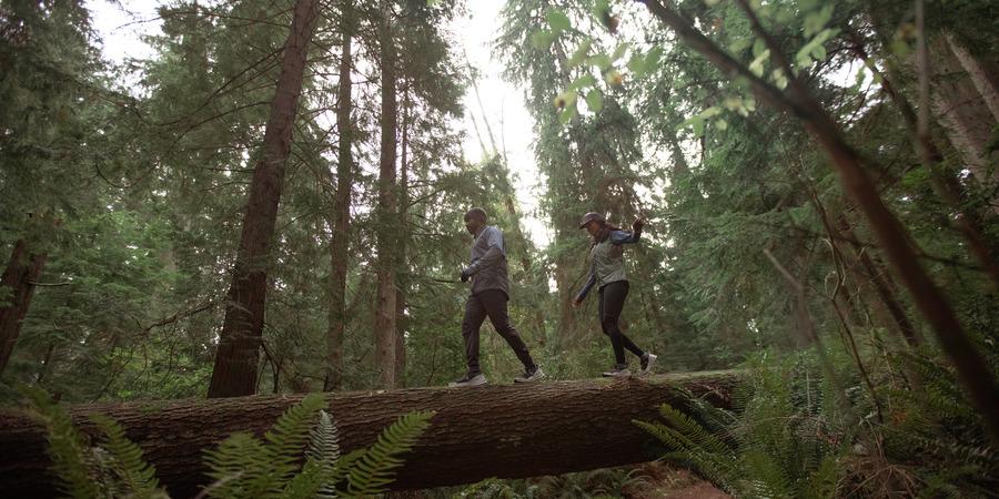 Two people trail running across a fallen tree.