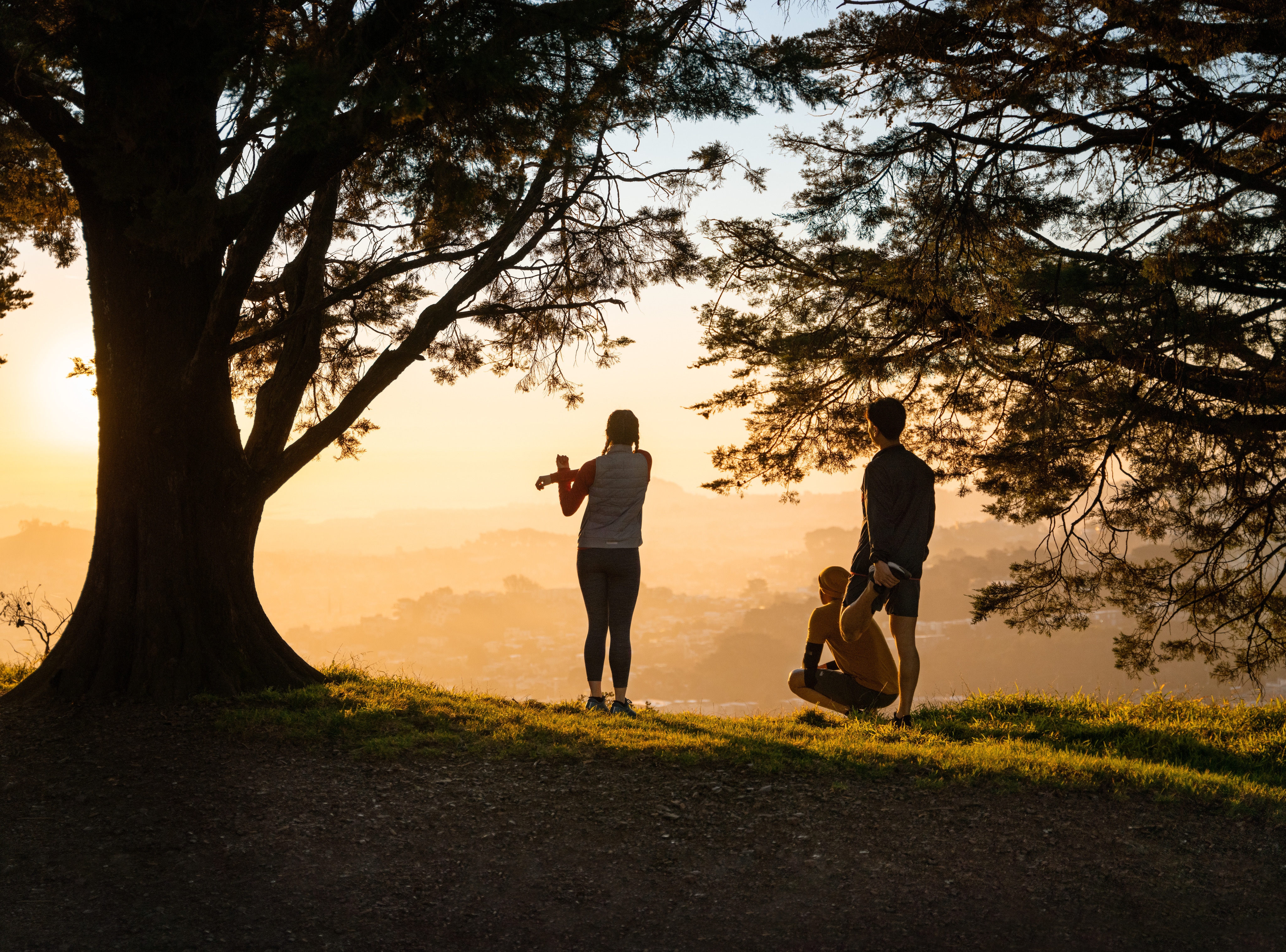 Three people stop to stretch while looking off into the distance as the sun begins to set.