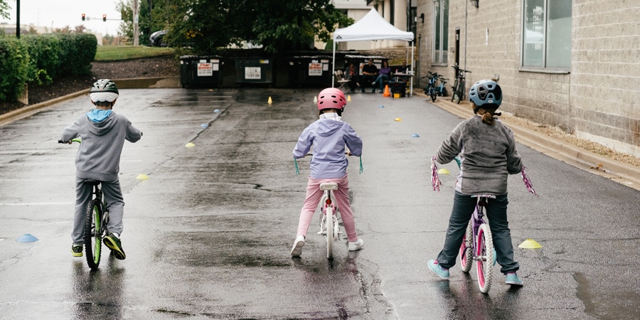 Tres niños practican scooting y deslizamiento en bicicletas sin pedales