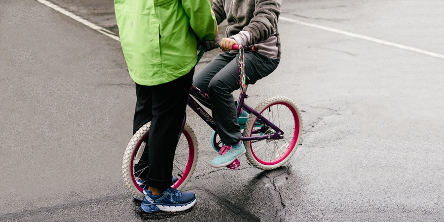 an adult keeping a bike steady while I child sits on it and balances